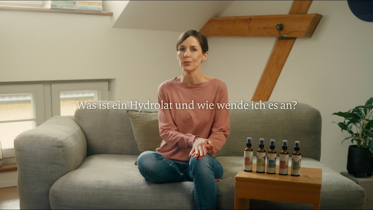 Frau sitzt auf grauem Sofa mit fünf Fläschchen Hydrolat auf Holztisch, natürliche Aromatherapie, Galerie Position 1, Schweizer Aromatherapie