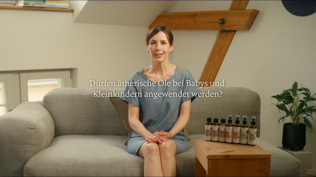 Frau sitzt auf grauem Sofa mit ätherischen Ölen auf Holztisch, helle Atmosphäre, Galerie Position 1, Schweizer Aromatherapie