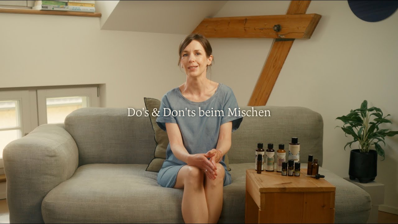 Frau sitzt auf grauem Sofa mit ätherischen Ölen auf Holztisch, Galerie Position 1, Schweizer Aromatherapie, vegane Rezepturen