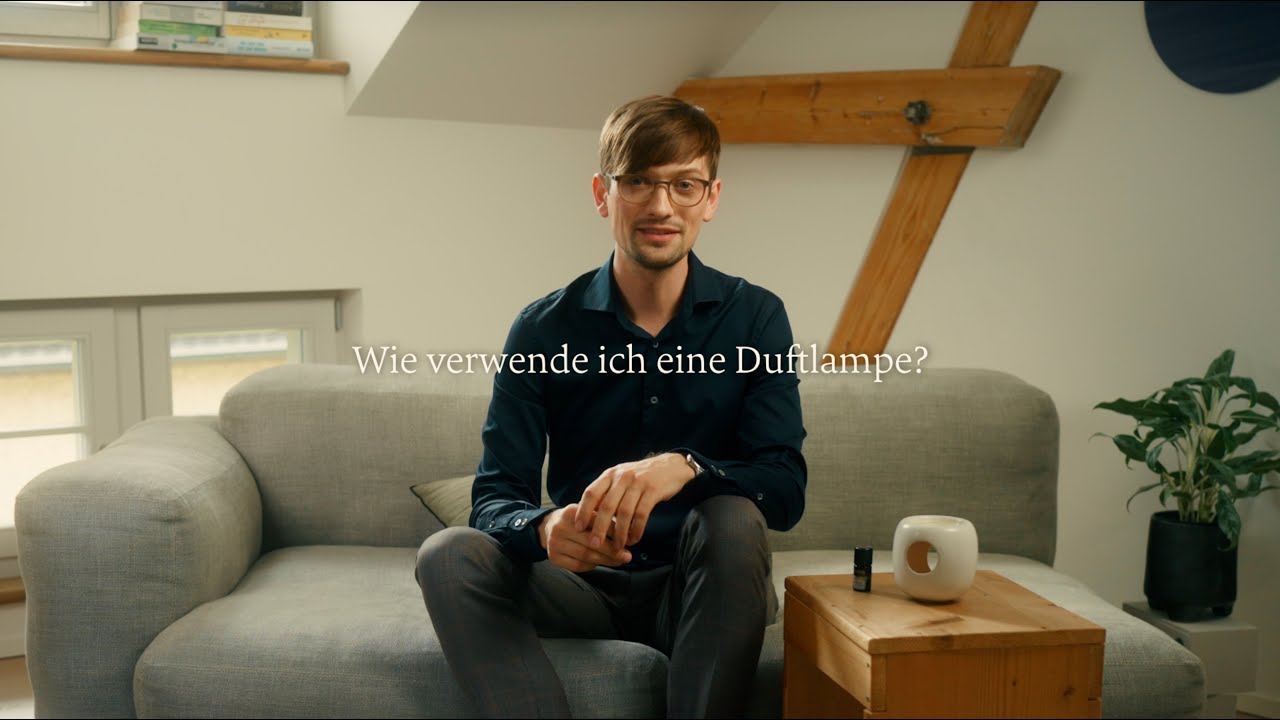 Mann sitzt auf grauem Sofa mit diffuser Lampe auf Holztisch, helle Wohnumgebung, Galerie Position 1, Schweizer Aromatherapie