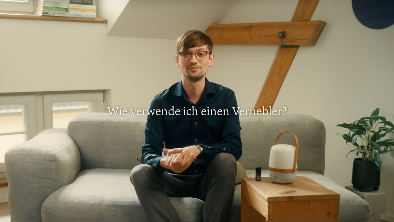 Mann sitzt auf grauem Sofa mit Vernebler und ätherischen Ölen, helle Wohnatmosphäre, Galerie Position 1, Schweizer Aromatherapie