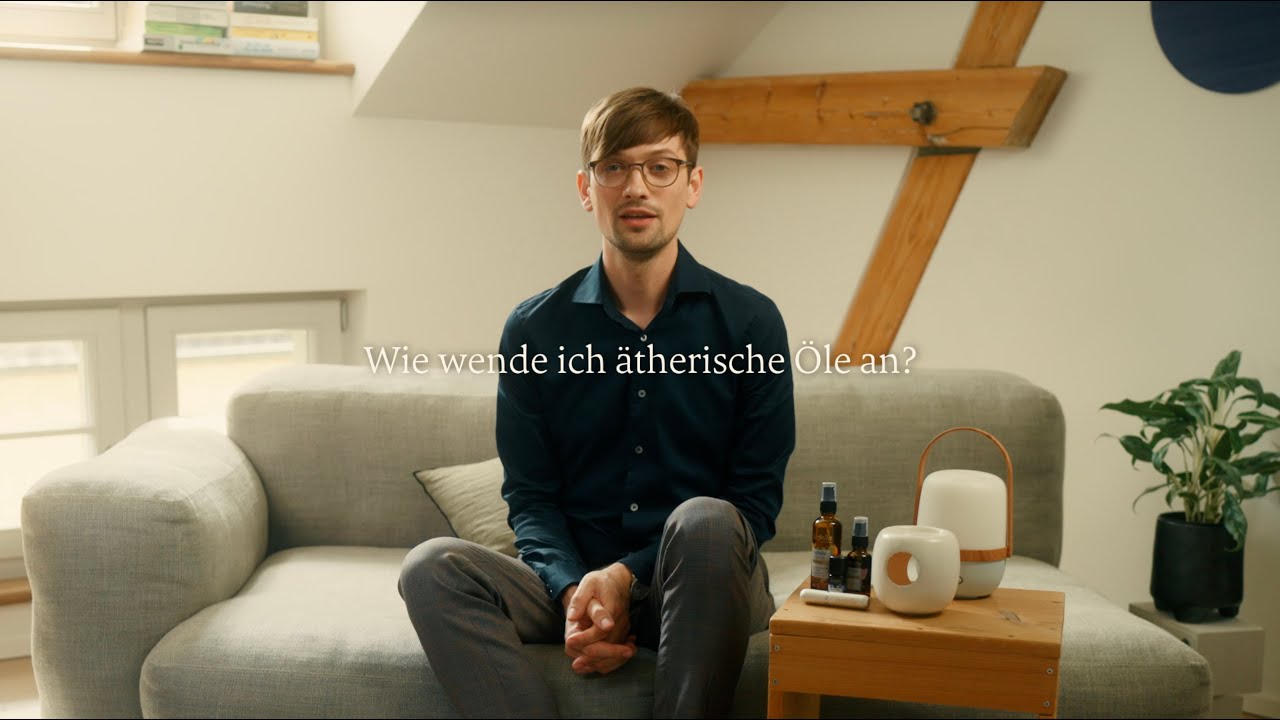 Mann sitzt auf grauem Sofa mit ätherischen Ölen und Diffuser auf Holztisch, helle Wohnumgebung, Galerie Position 1, Schweizer Aromatherapie