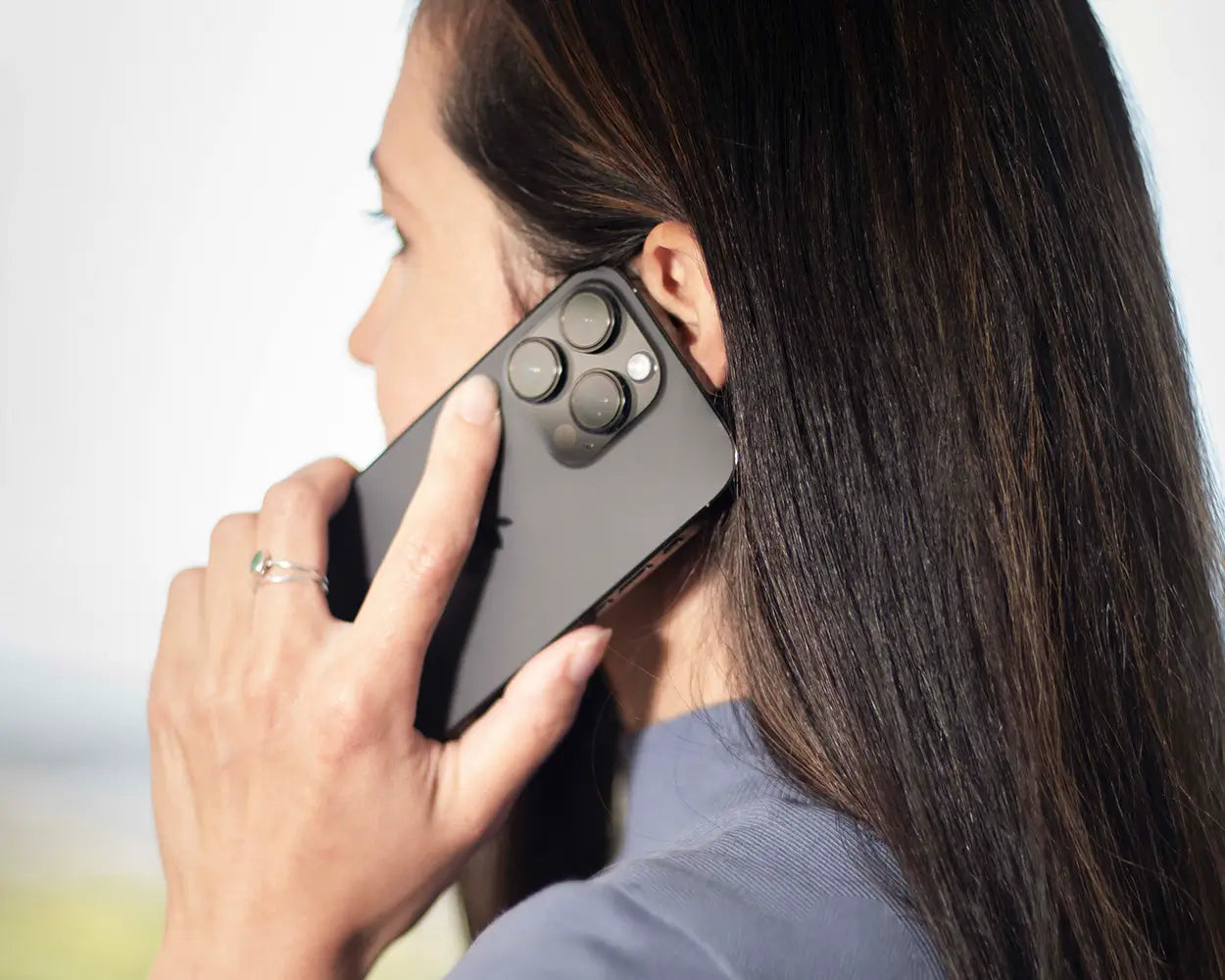 Frau mit langen braunen Haaren hält Smartphone ans Ohr, helle Umgebung, Galerie Position 1, Schweizer Aromatherapie.