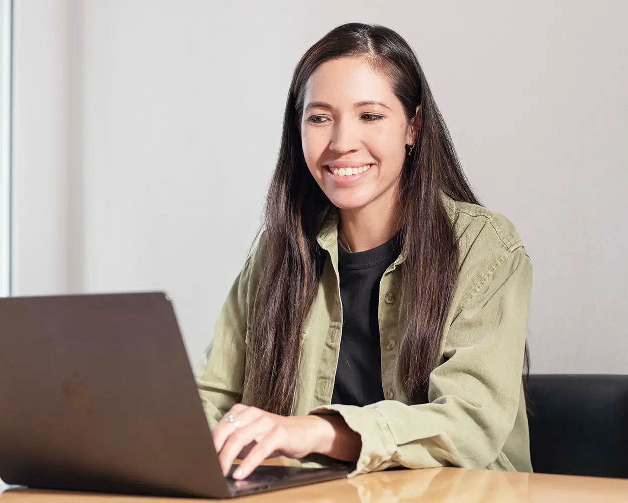 Frau mit langem braunen Haar arbeitet am Laptop an neutraler Wand, Galerie Position 1, Schweizer Aromatherapie, Naturkosmetik