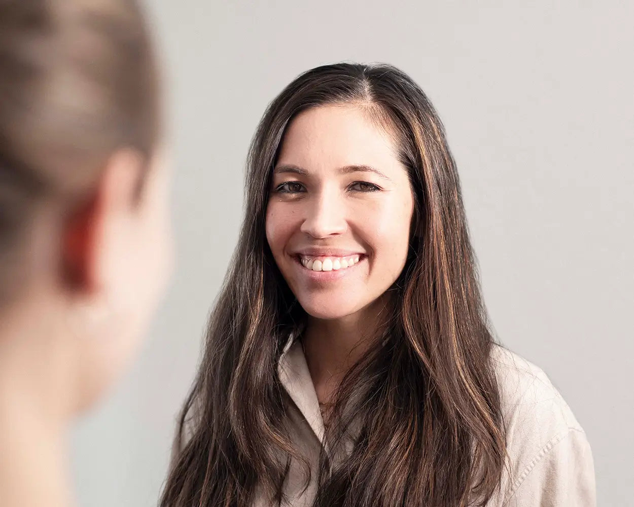 Frau mit langen braunen Haaren lächelt freundlich, neutrale Wand im Hintergrund, Galerie Position 1, Schweizer Aromatherapie.