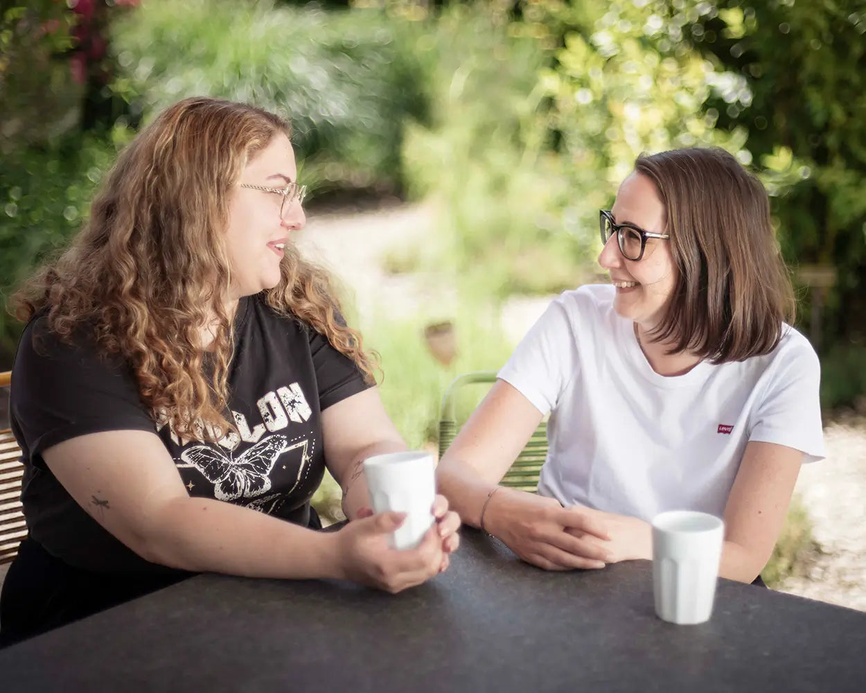 Zwei Frauen mit Brille sitzen entspannt an Tisch im Garten, natürliche Umgebung, Galerie Position 1, Schweizer Aromatherapie