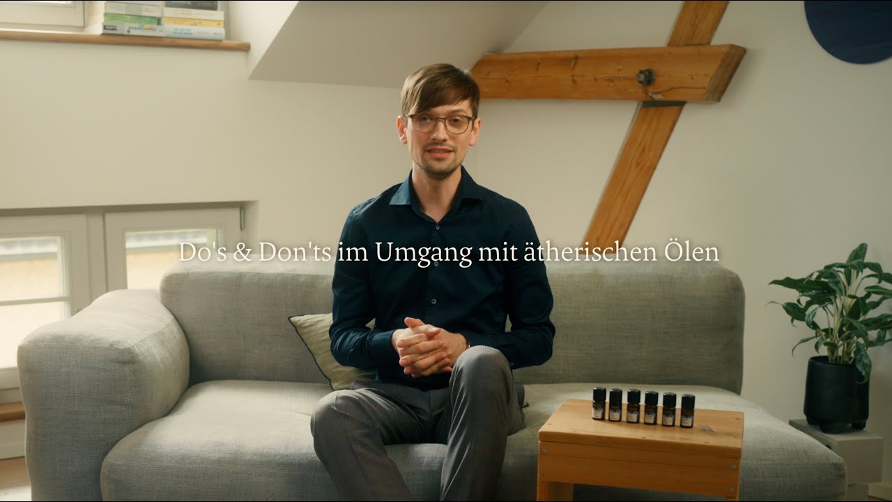 Mann sitzt entspannt auf grauem Sofa mit ätherischen Ölen auf Holztisch, Galerie Position 1, Schweizer Aromatherapie