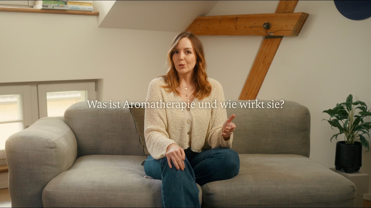 Frau sitzt auf grauem Sofa in natürlichem Wohnraum mit Pflanzen, Galerie Position 1, Schweizer Aromatherapie zertifizierte Naturkosmetik