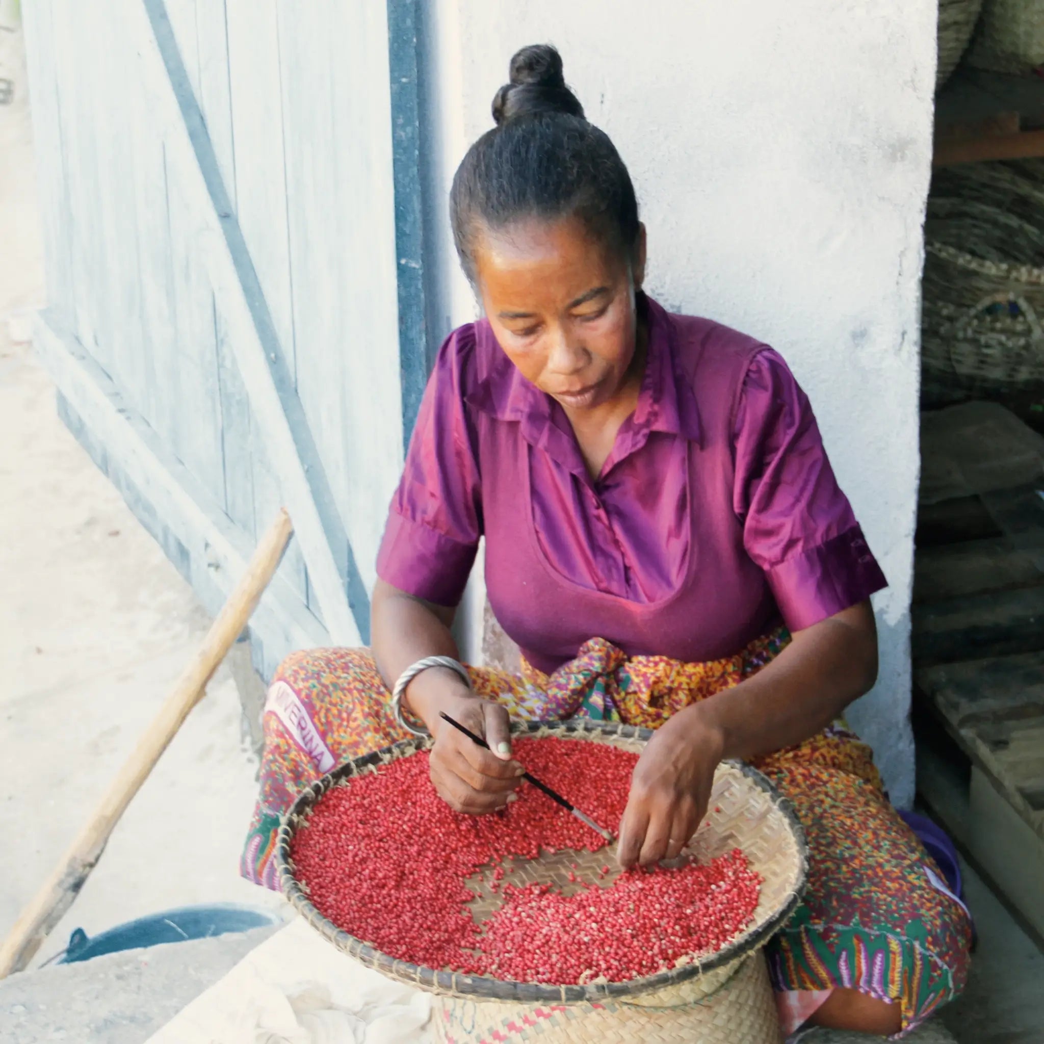 Frau sortiert rote Samen in Korb sitzend vor Holztür, Galerie Position 1, Schweizer Aromatherapie, vegane Rezepturen