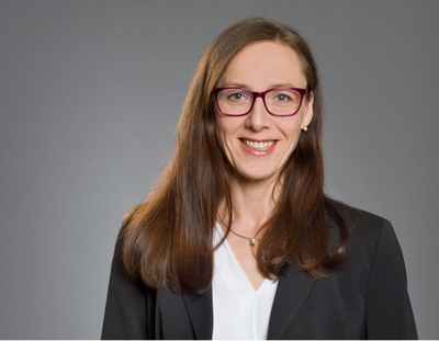 Porträt einer Frau mit braunen Haaren, roter Brille und schwarzem Blazer vor grauem Hintergrund, Galerie Position 1, Schweizer Aromatherapie