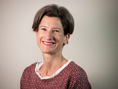 Frau mit kurzem braunem Haar und rotem Musterpullover lächelnd vor beigem Hintergrund, Galerie Position 1, Schweizer Aromatherapie