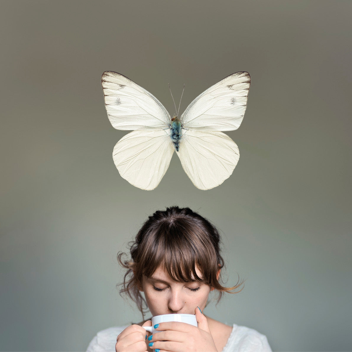 Junge Frau trinkt Tee vor grauem Hintergrund mit großem weißen Schmetterling über ihrem Kopf, Galerie Position 1, Schweizer Aromatherapie
