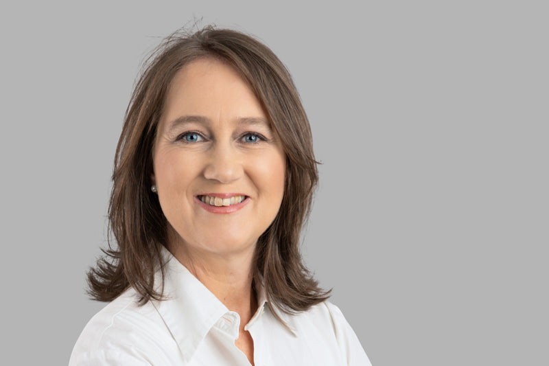 Porträt einer lächelnden Frau vor grauem Hintergrund, Galerie Position 1, Schweizer Aromatherapie, zertifizierte Naturkosmetik.