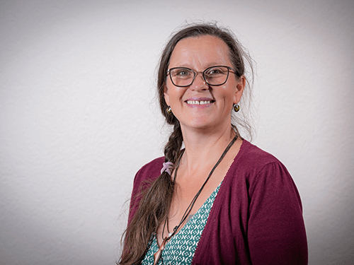 Frau mit Brille, lächelnd, im grünen gemusterten Top und bordeauxrotem Cardigan, Galerie Position 1, zertifizierte Naturkosmetik