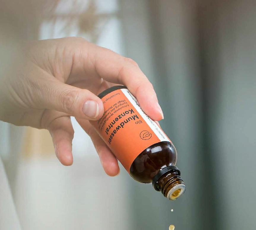 Hand hält braune Flasche mit Bio Mundwasser, Tropfen fallen heraus, Galerie Position 1, Schweizer Aromatherapie, zertifizierte Naturkosmetik