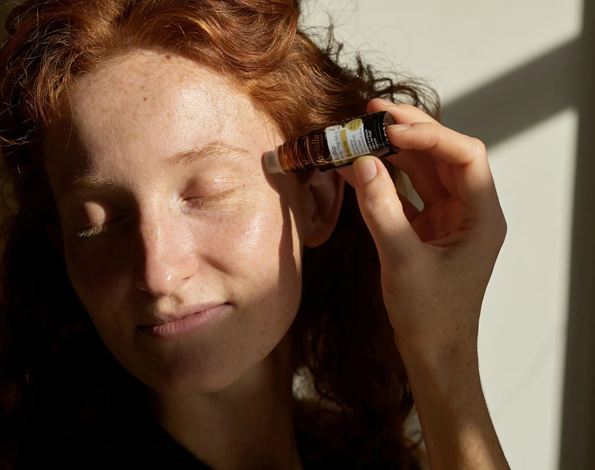 frau mit roten haaren trägt ätherisches öl an schläfe auf, galerie position 1, Schweizer Aromatherapie, zertifizierte Naturkosmetik