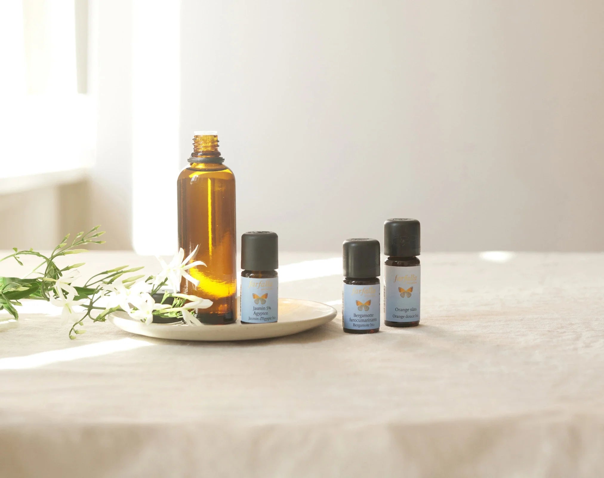 Braunes Glasfläschchen mit drei kleinen blauen Aromaölflaschen auf hellem Stoff, Galerie Position 1, Schweizer Aromatherapie, zertifizierte Naturkosmetik.