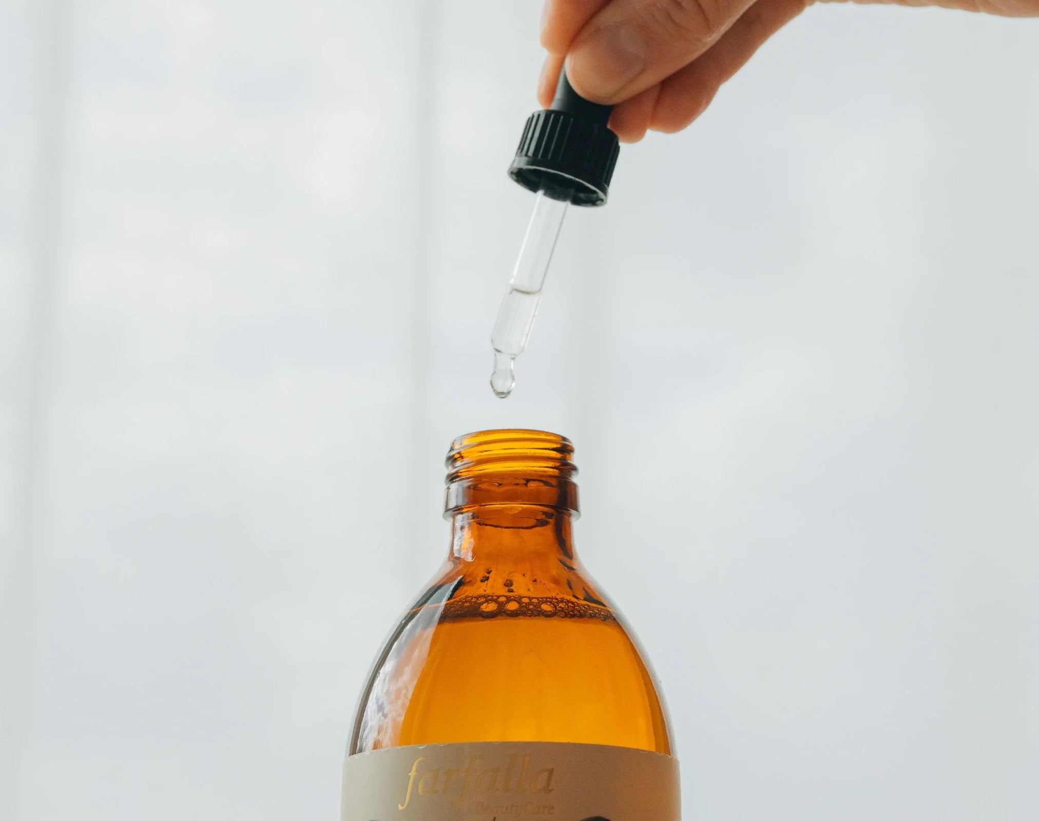 Hand hält Tropfpipette mit Tropfen über braunem Fläschchen, Galerie Position 1, Schweizer Aromatherapie, Bio ätherische Öle.