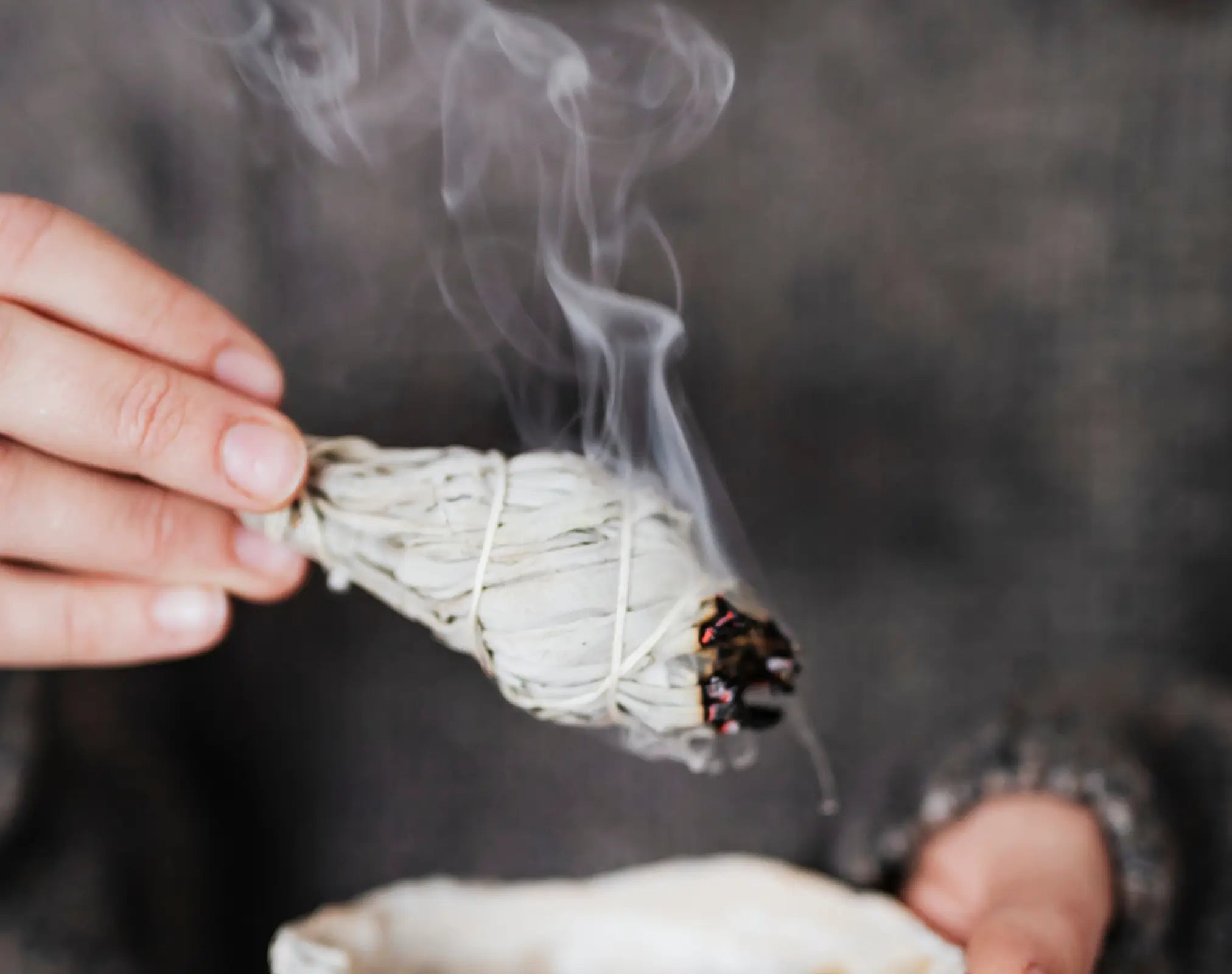 Hand hält brennenden weißen Salbeibündel mit aufsteigendem Rauch, Galerie Position 1, Schweizer Aromatherapie, zertifizierte Naturkosmetik