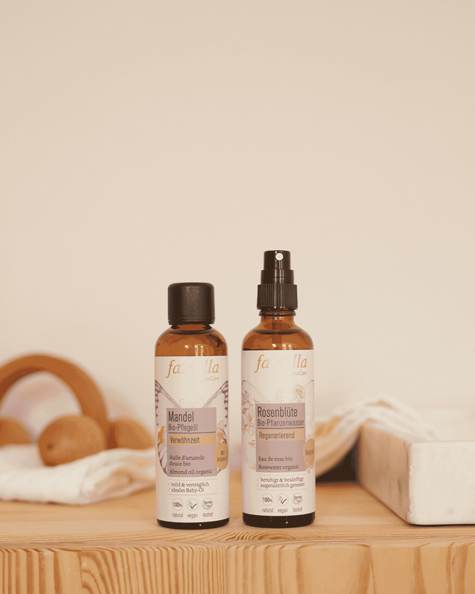 Zwei Farfalla Bio Pflegeöle Mandel und Rosenblüte auf Holz mit weißem Stoff und Deko, Galerie Position 1, Schweizer Aromatherapie.