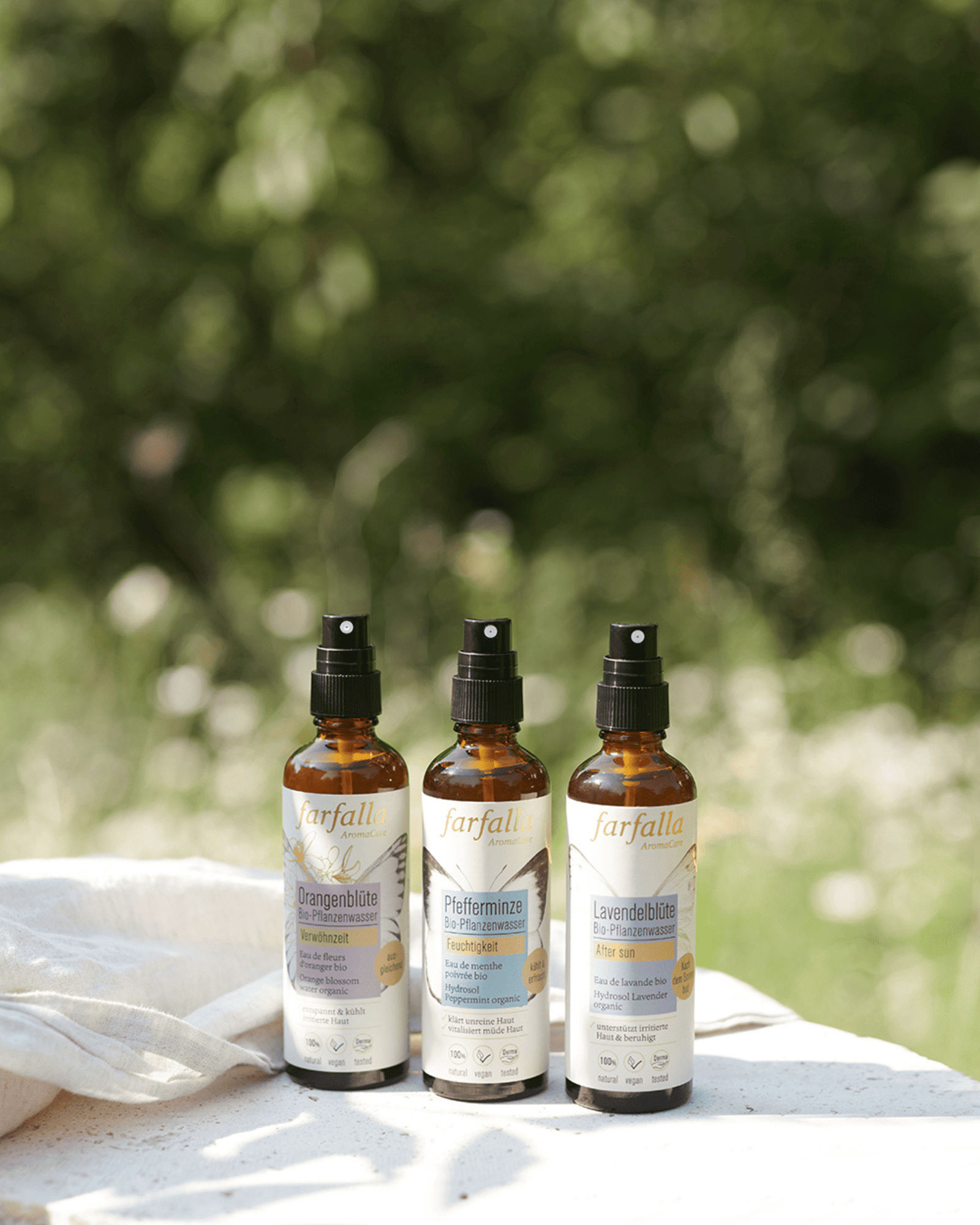 Drei farfalla Aromawässer auf hellem Untergrund mit grünem unscharfem Hintergrund, Galerie Position 1, Schweizer Aromatherapie, Bio ätherische Öle, vegane Rezepturen, zertifizierte Naturkosmetik