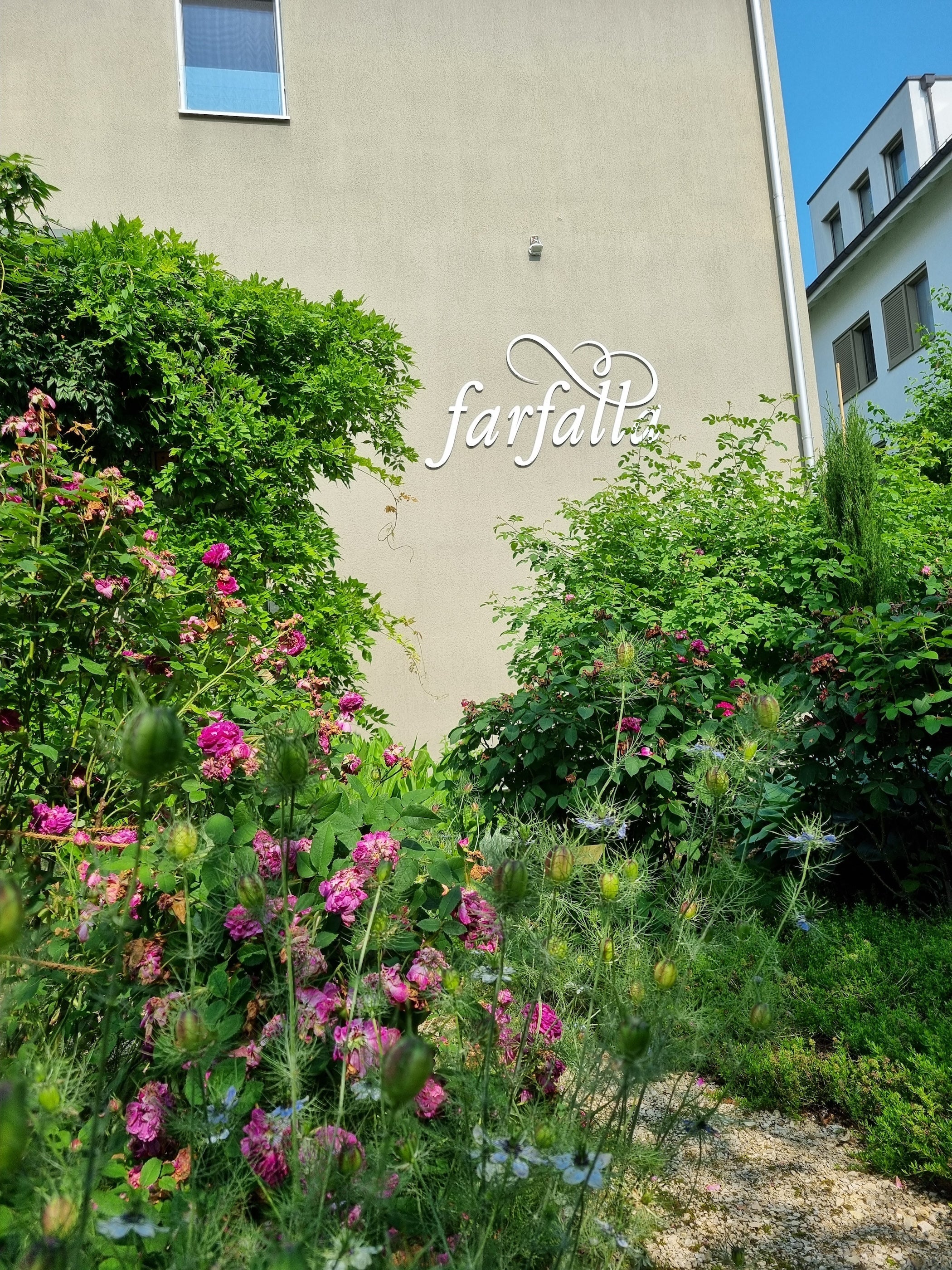 Fassade mit farfalla Schriftzug und blühendem Garten bei Sonnenschein, Galerie Position 1, Schweizer Aromatherapie.