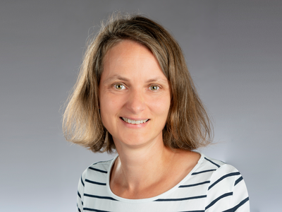 Porträt einer Frau mit kurzem braunem Haar und gestreiftem Shirt vor neutralem Hintergrund, Galerie Position 1.