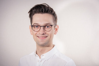 Porträt junger Mann mit Brille vor hellem Hintergrund, Galerie Position 1, zertifizierte Naturkosmetik Schweiz, vegane Rezepturen