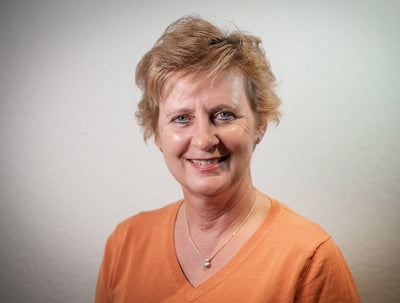 Porträt einer lächelnden Frau mit kurzem blondem Haar vor hellem Hintergrund, Galerie Position 1, Schweizer Aromatherapie, vegane Rezepturen, zertifizierte Naturkosmetik