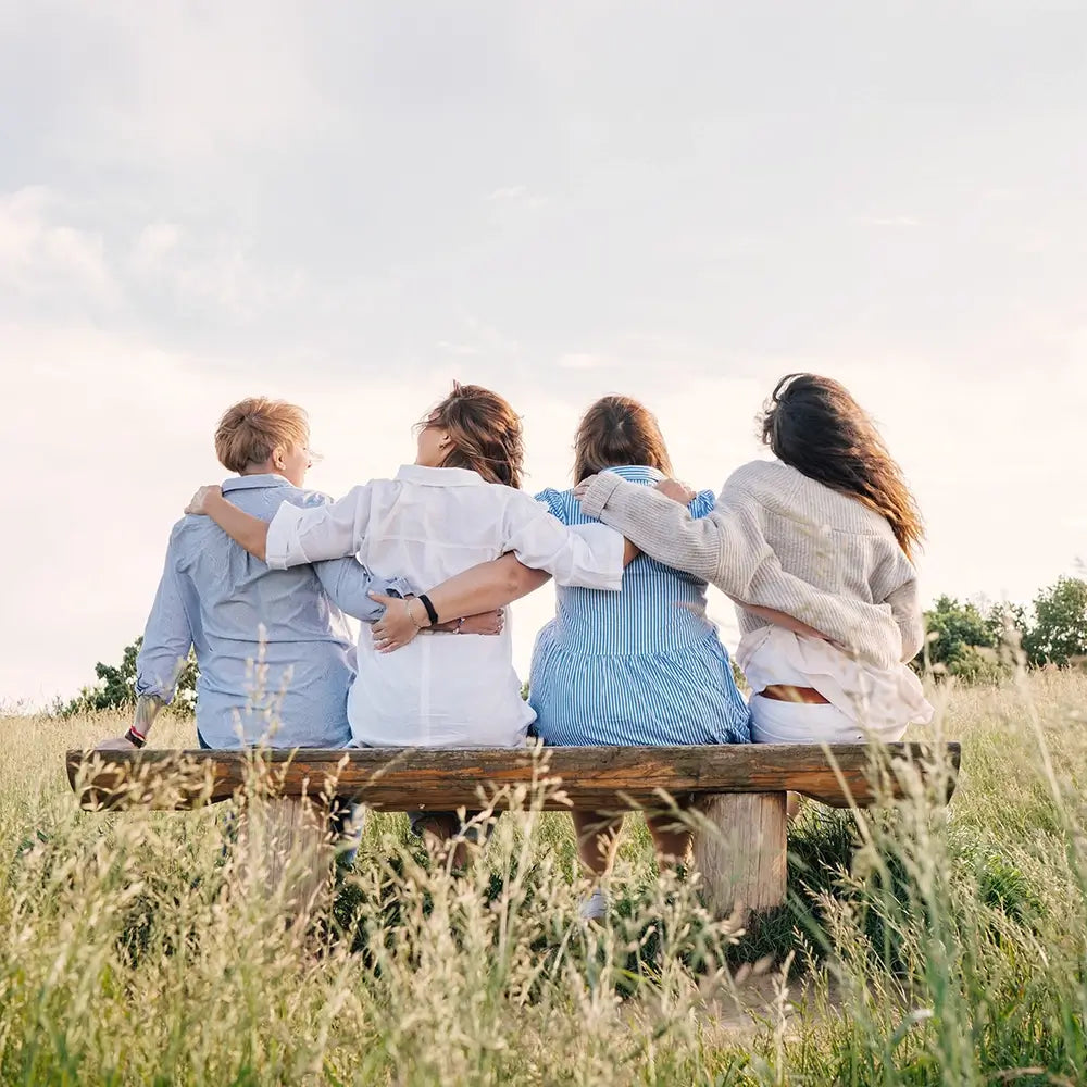 Vier Personen sitzen Arm in Arm auf Holzbänkli im Grünen, offene Landschaft, Galerie Position 1, Schweizer Aromatherapie